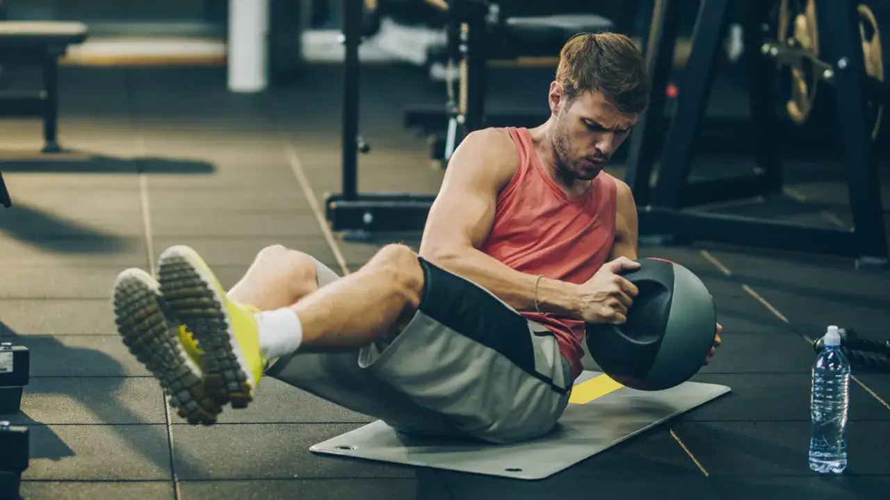 Uomo esegue russian twist con palla medica su un tappetino in palestra, concentrato sull'esercizio per addominali.