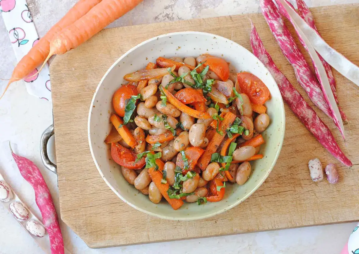 Insalata colorata con fagioli borlotti, carote e pomodorini, guarnita con erbe fresche.