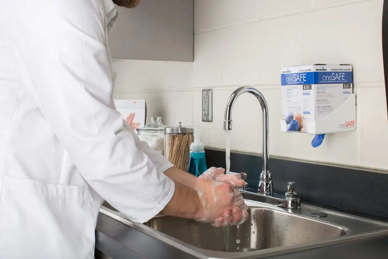 Un medico in camice bianco si lava le mani insaponate sotto un rubinetto. Prevenire il virus intestinale 2026.