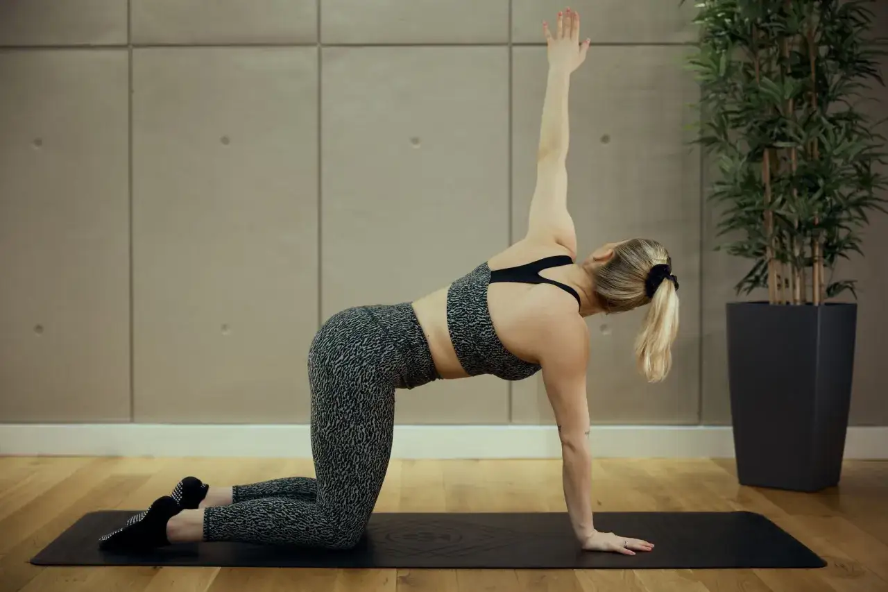 Donna in posa di pilates su un tappetino, con un braccio alzato. Il pilates fa dimagrire tonificando il corpo.
