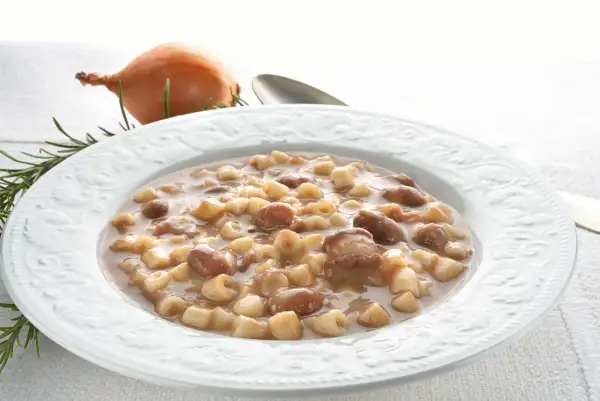 Piatto di pasta e fagioli borlotti, con cipolla e rosmarino sullo sfondo. Un comfort food che scalda il cuore.