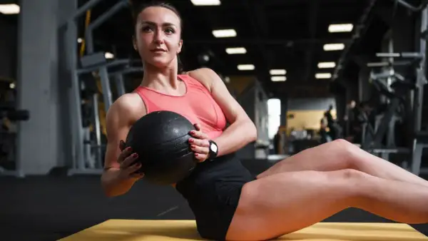Donna esegue russian twist con palla medica in palestra, concentrata sull'allenamento addominale.