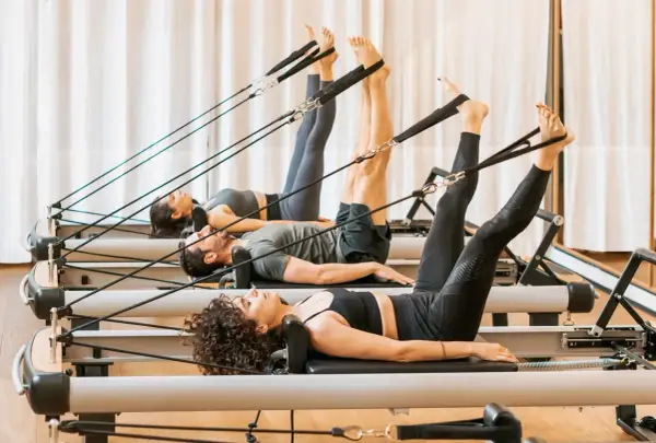 Persone in posa sul pilates reformer, scopri cos'è questo attrezzo per un allenamento completo.