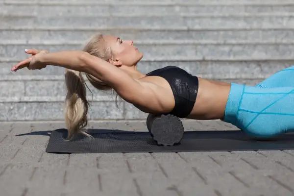 Donna bionda usa un foam roller schiena per rilassare i muscoli dopo l'allenamento.