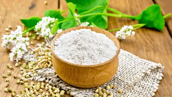 Farina di grano saraceno in ciotola, chicchi e fiori. Un alimento utile per chi soffre di colon irritabile.