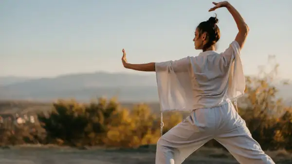 Donna pratica tai chi all'aperto, con le braccia sollevate e il corpo in posizione di equilibrio, immersa nella luce dorata del tramonto.