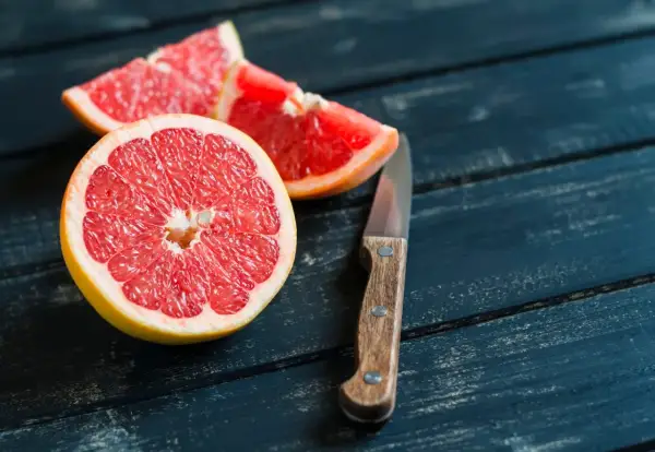 Mezzo pompelmo succoso e spicchi su un tavolo di legno scuro, pronti per essere gustati a stomaco vuoto.
